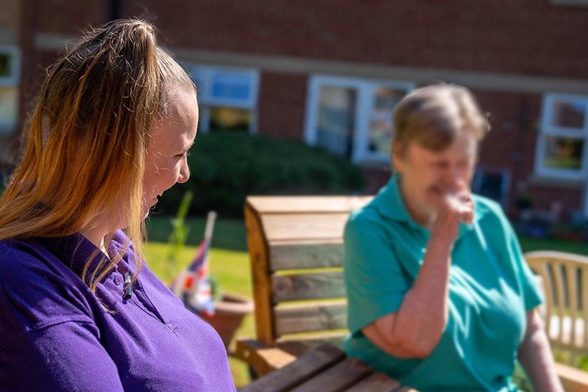 Sanctuary Care staff and resident sitting on a bench outside having a conversation