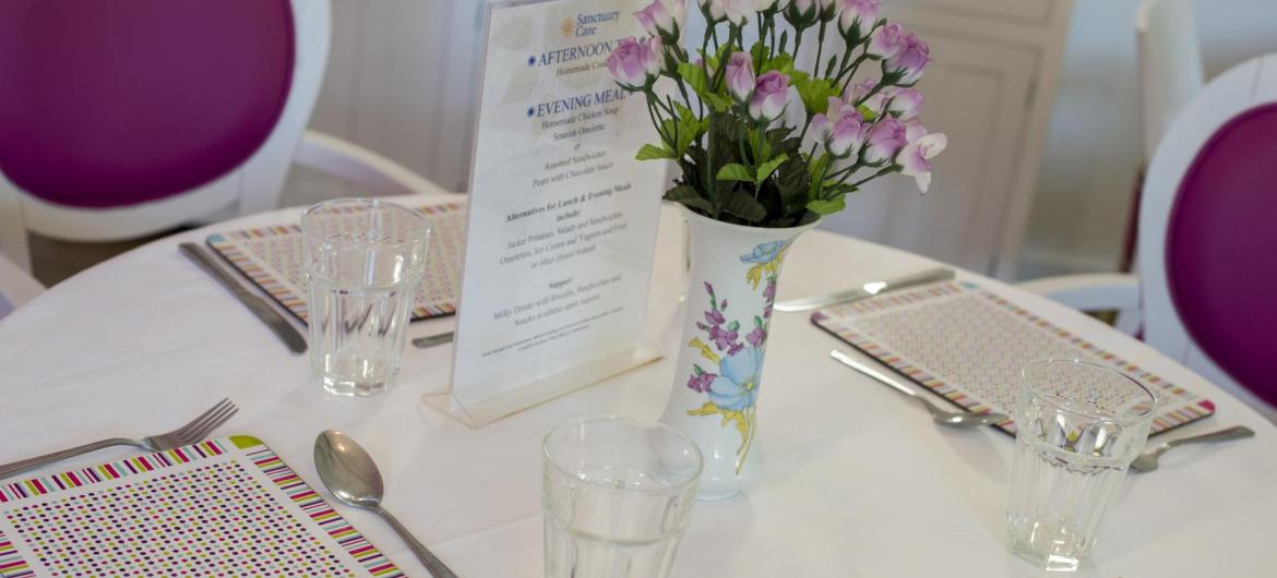A dining table at the Parkview House Residential Care Home with simple place settings, tumblers and flowers in a vase.