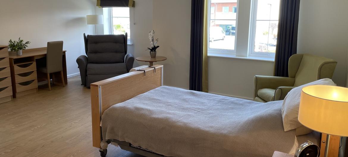 A cosy bariatric bedroom furnished with a bed, chairs and a desk