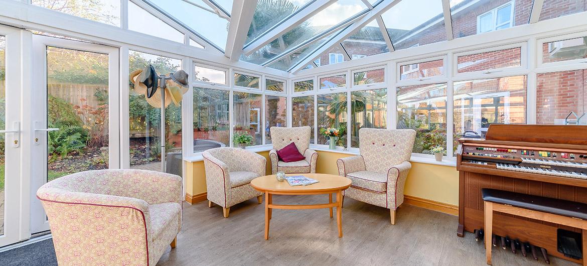 Beautiful conservatory with armchairs and a piano at Wantage Care Home in Oxfordshire