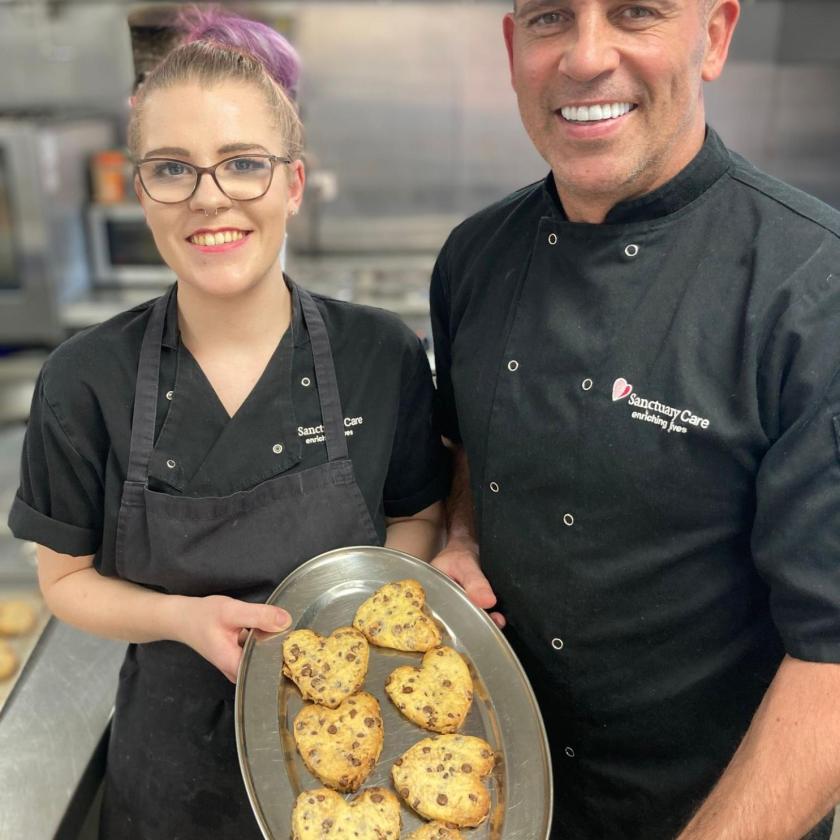 Kitchen Assistant Vicky and Chef Manager Jason holding a tray of heart shaped cookies 