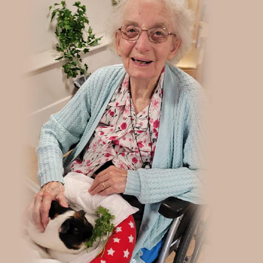 Resident, Eva Poore, smiling with a guinea pig on her lap