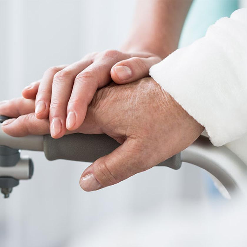 A carer's hand rests on a resident's hand on their walking frame