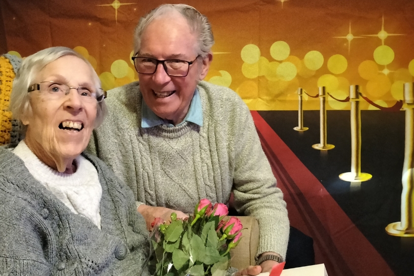 Married residents sat down smiling together holding a bunch of flowers