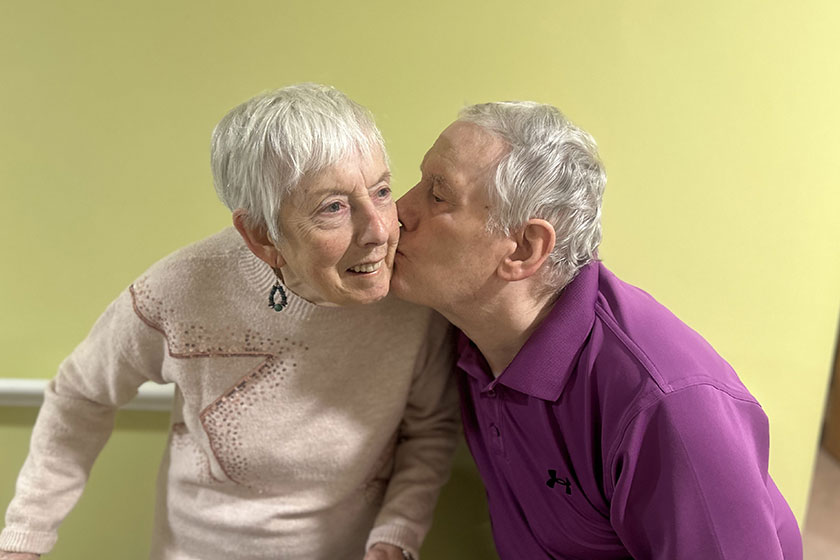 Married residents standing with the male kissing the female on the cheek