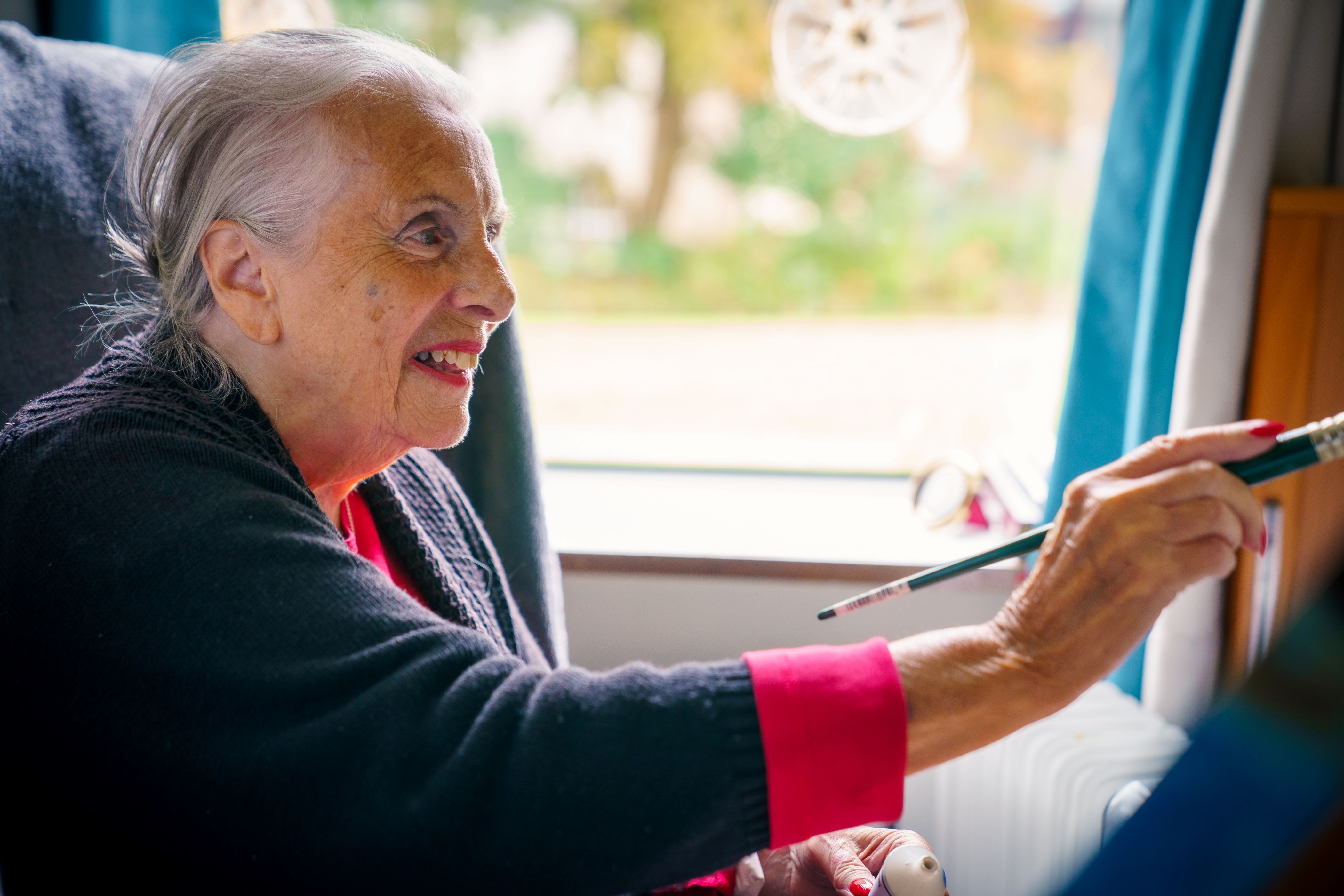 An elderly woman sitting on a sofa and smiling while painting with a paint brush