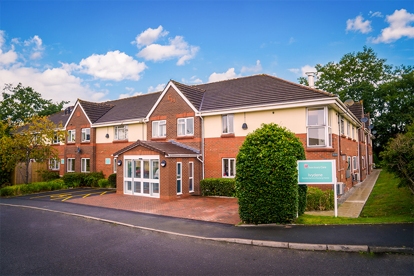 Exterior of a red brick building with white accents. In the foreground is a sign that states 'Ivydene Residential and Nursing Home'