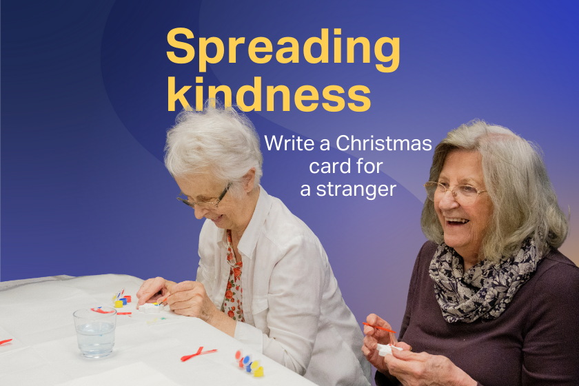 Two female residents doing crafts at a table and laughing. Text above reads 'Spreading kindness - write a Christmas card for a stranger'