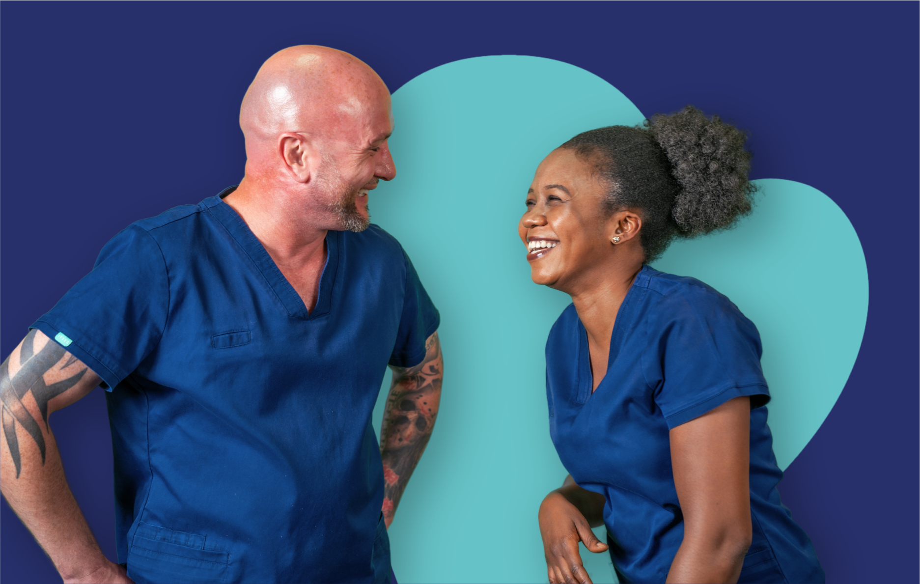 Two people in blue scrubs standing together and facing each other in front of a large heart shape on a dark blue background.
