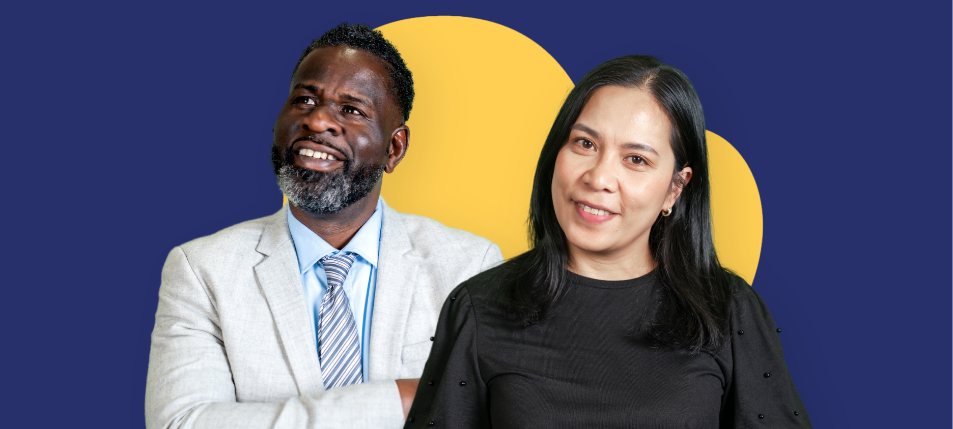 Two people standing in front of a large yellow heart shape on a dark blue background. One person is wearing a light-coloured suit and the other is wearing a black top. Both are facing the camera.