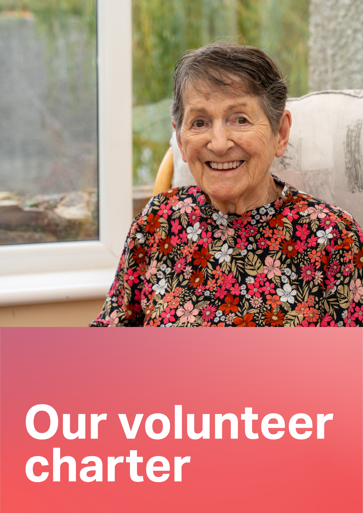 An older person sitting by a window and smiling, wearing a floral patterned top. Text "Our volunteer charter" underneath the picture.