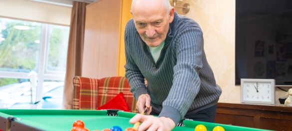A resident smiling and playing pool in a well lit care home day care centre