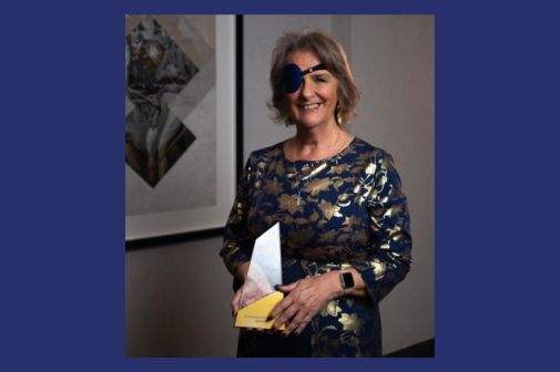 A woman in a blue and gold evening dress proudly holding an award