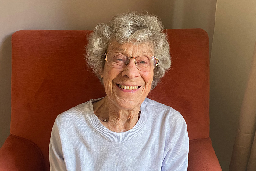 Jean, resident at Juniper House Care Home in Worcester, sits in a chair and smiles.