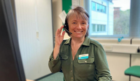 A female Sanctuary Care employee is smiling. She wears a phone headset and is ready to take a call.