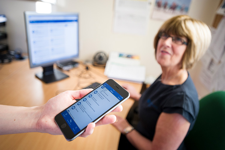 Jill Pearce sat at her desk with a mobile phone being held in the foreground