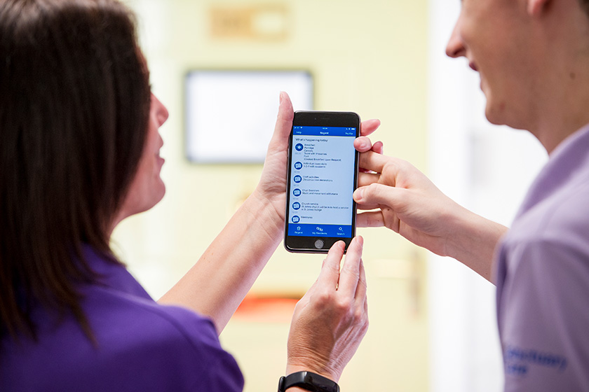 Two Sanctuary Care staff members holding a mobile phone with the kradle care app visible