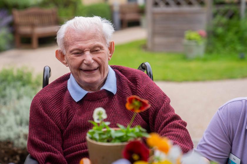 A male resident sat potting a plant and smiling in the garden