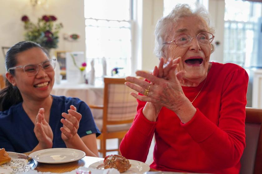 A resident and member of staff sat at a table and clapping happily