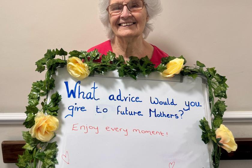 Resident Marlene holding a whiteboard with the advice to mothers saying enjoy every moment.