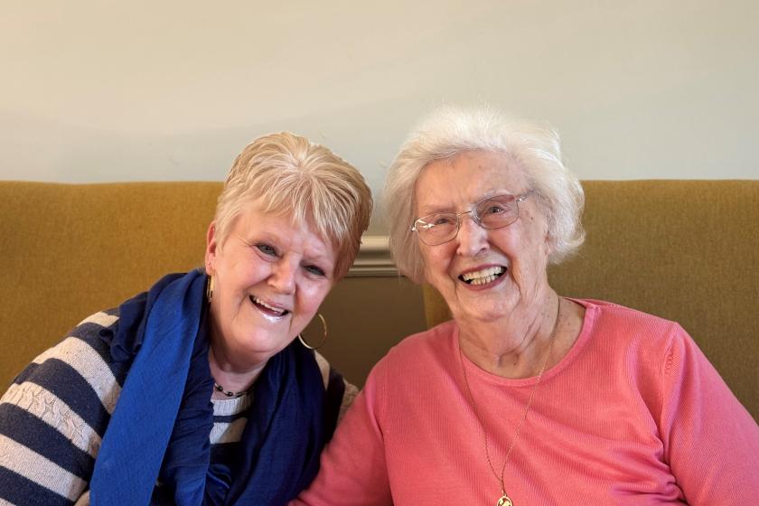 A female resident and her daughter sat next to each other on a sofa and smiling 