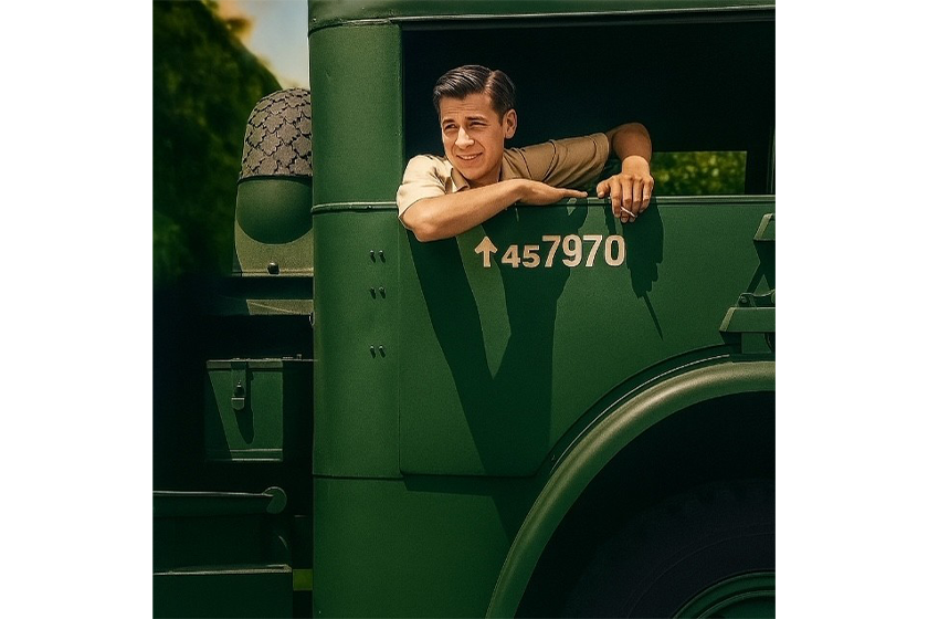 A young man leans out of the window of a green military-style truck, smiling.