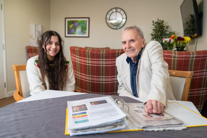A young visitor with a resident sat at a table together and smiling at the camera