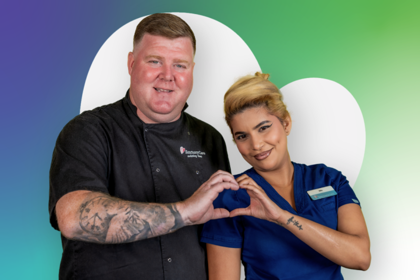 Two people standing together and making a heart shape with their hands against a green and blue background with large white heart shape