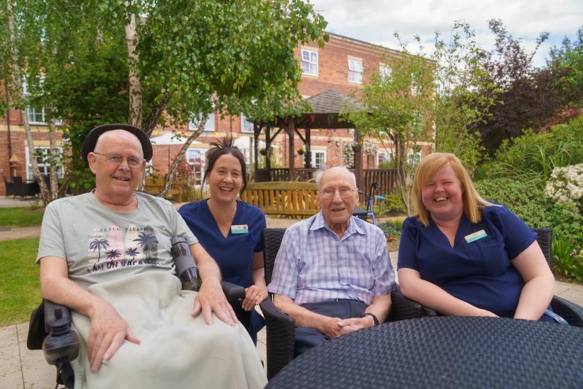 Two residents and two carers sat together outside at a Veteran Friendly event in a care home garden