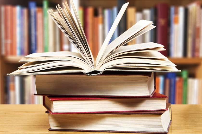 A stack of books rest on a desk in a library.