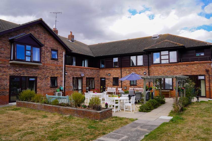 Exterior image of Don Thomson House Residential Care Home with blue sky and clouds in the sky and tables and chairs outside