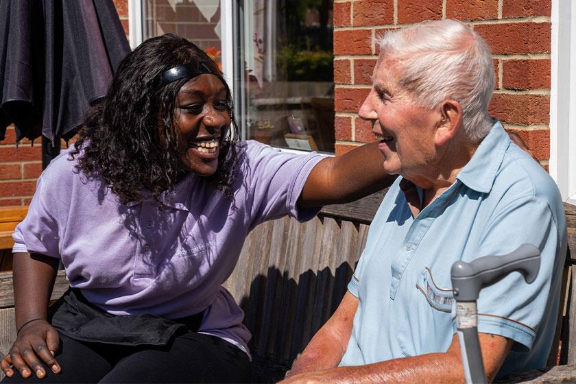 A care assistant puts her arm around a resident while sat outside