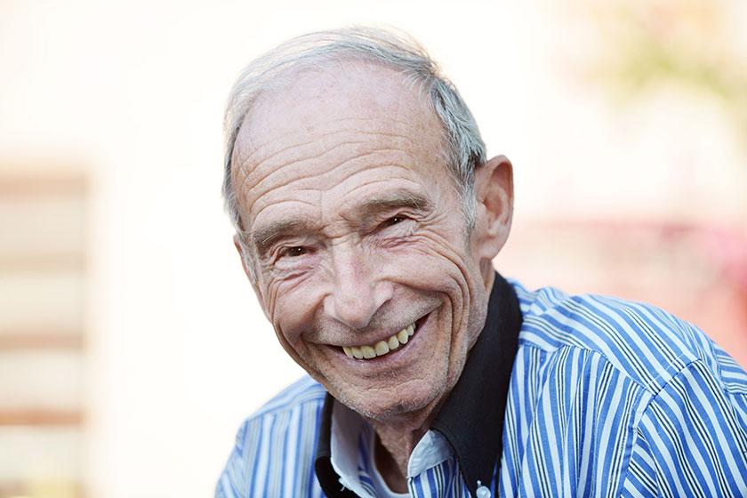 Elderly man wearing a striped shirt smiles as he has his photo taken