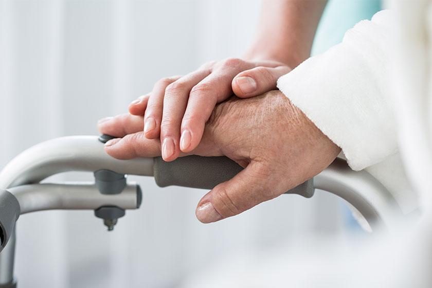 A carer's hand rests on a resident's hand on their walking frame