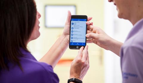 Two Sanctuary Care staff members holding a mobile phone with the kradle care app visible