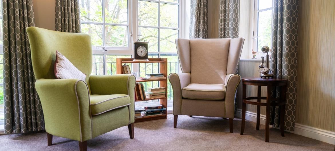 Two comfortable arm chairs in a well lit room next to a floor to ceiling window