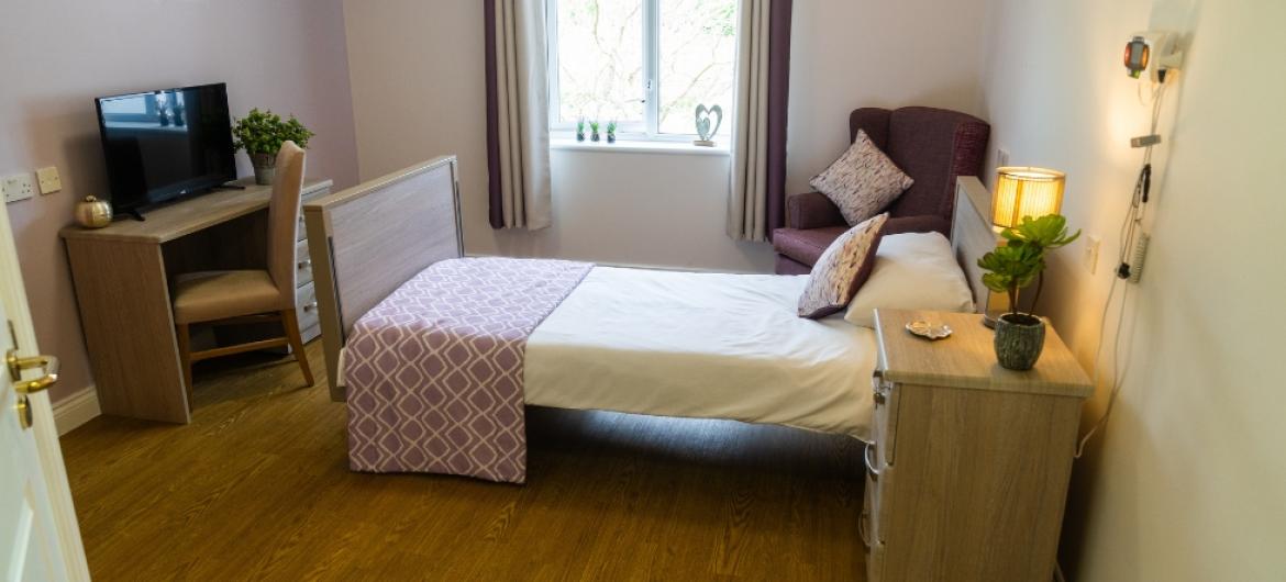 A cosy single bedroom with a tv, armchair and bedside table