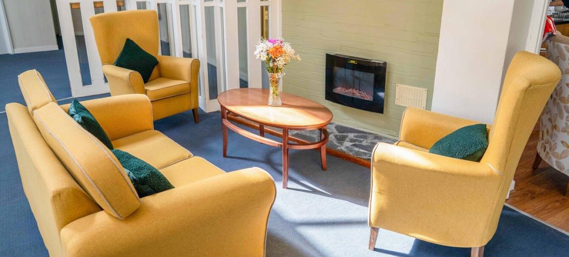 A vibrant yellow sofa with two matching arm chairs located around a wall mounted electric fire.