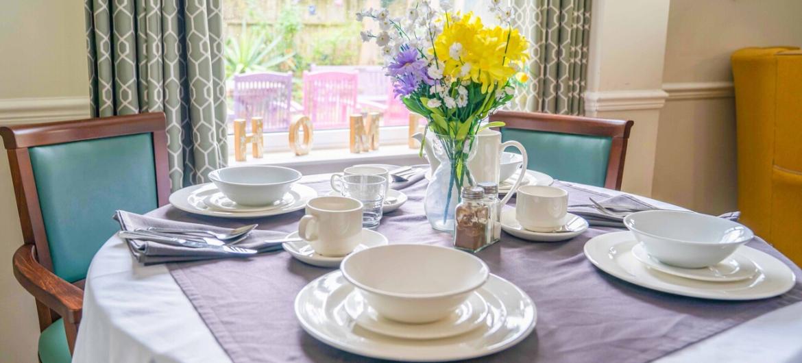 A bright and welcoming dining area at The Trevern with a neatly set table, cheerful flowers, and comfy chairs to feel warm, social, and homely.