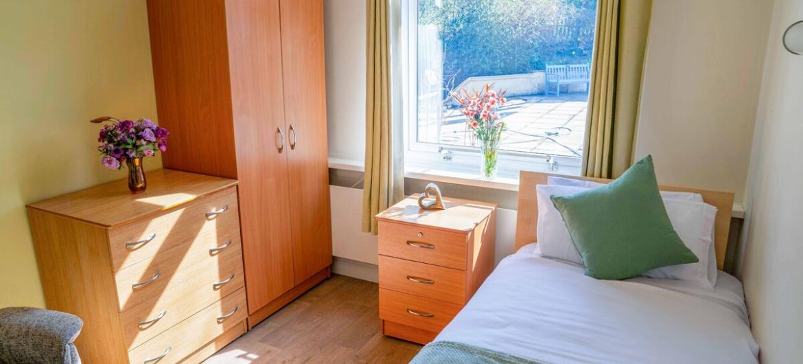 A calm, welcoming bedroom with soft natural light, a comfortable single bed, and homely wooden furniture. A peaceful space designed for comfort and ease.