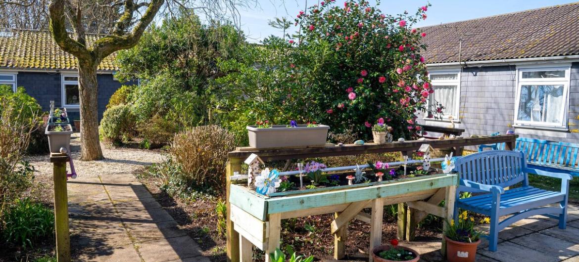 A beautiful garden with comfortable blue benches. The paved paths are easy to navigate, creating a peaceful, accessible space where residents can relax and enjoy the outdoors.