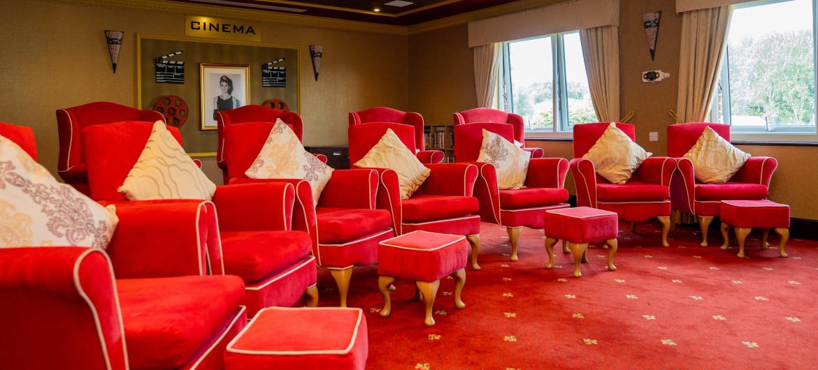A large cinema room with a semi circle of comfortable red armchairs and foot rests