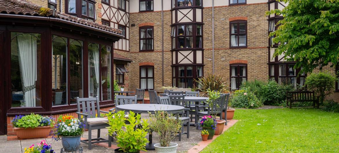 Exterior of a purpose built care home with patio tables and a lush green lawn