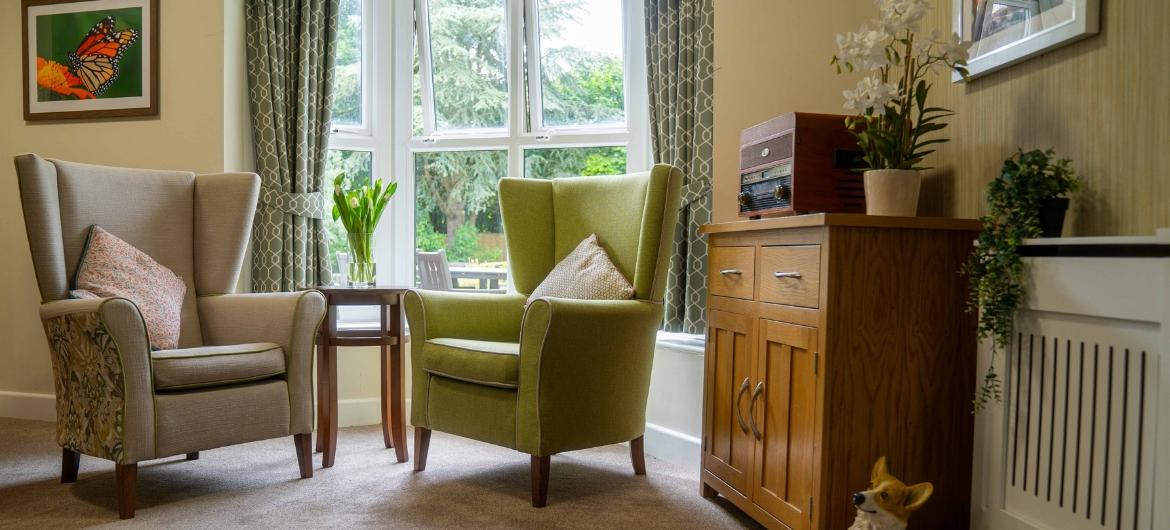A cosy corner of a care home with comfortable arm chairs infront of a window