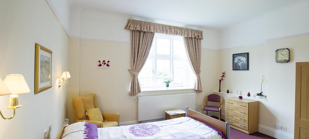 A pretty bedroom at The Winsor Nursing Home with soft lighting and coordinating home furnishings.