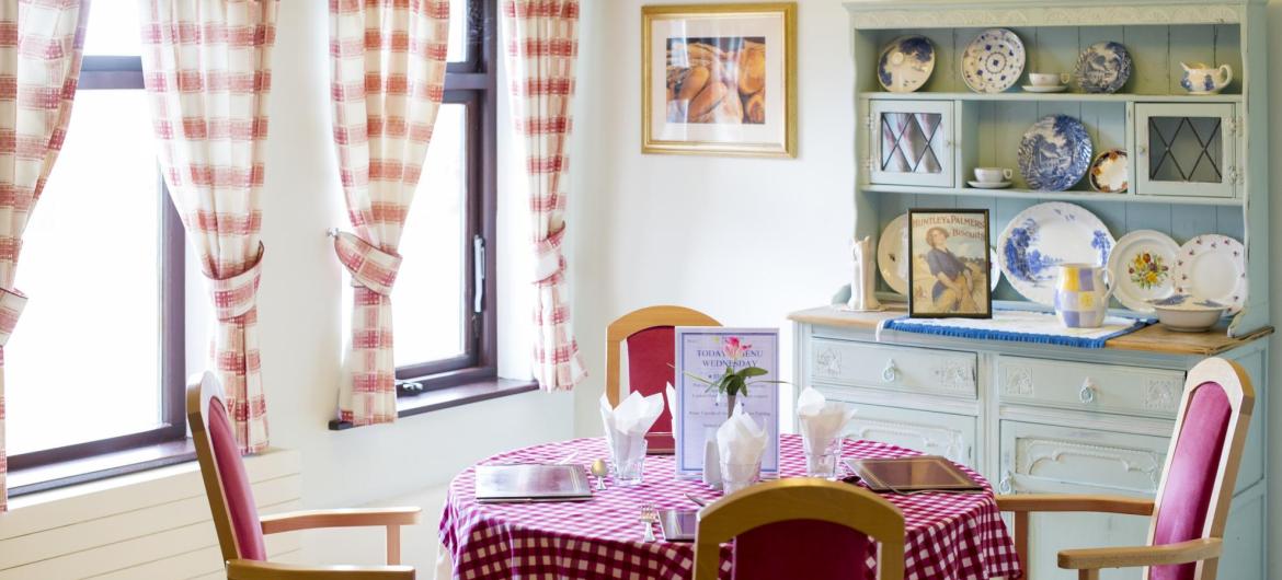 The country style dining room at Lyons Court Residential Care Home has chequered table cloths and a blue dresser.