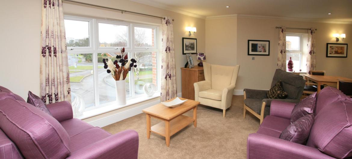 The light and airy lounge at Highcroft Hall Residential Care Home with comfy sofas, flowers and soft lighting.