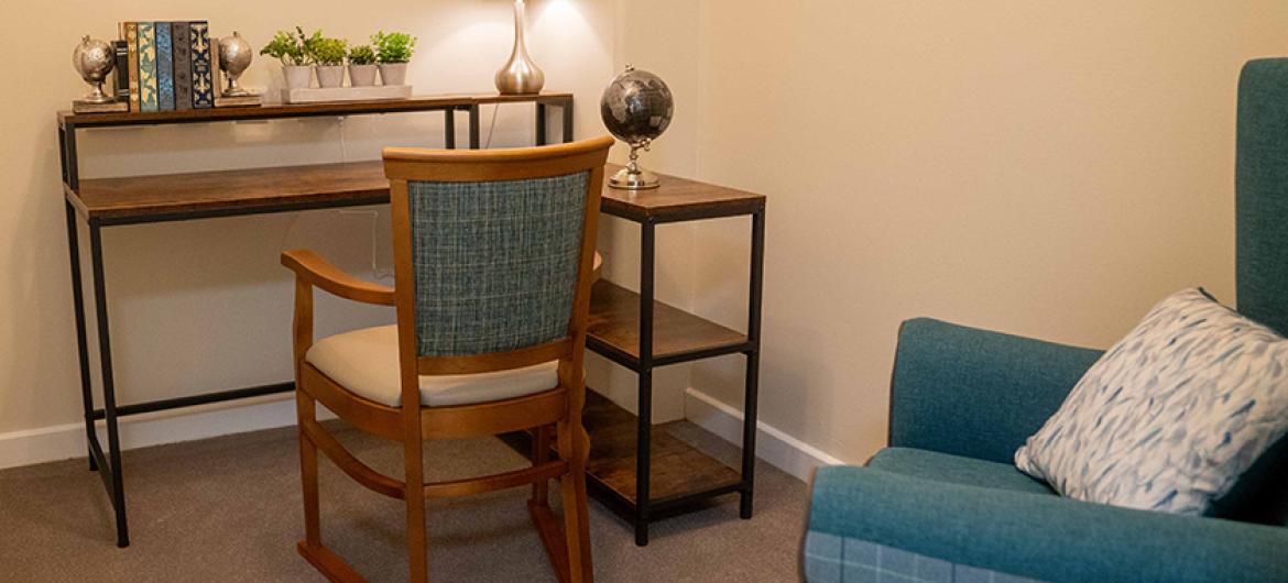 A desk nook housing a metal and wooden desk with matching shelving to the right and a brown wooden arm chair that tucks neatly underneath.