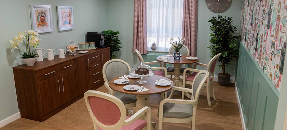 Cosy dining area nook located in an elongated room with two four person circular wooden dining seating areas. Dressed ready for a meal serving.