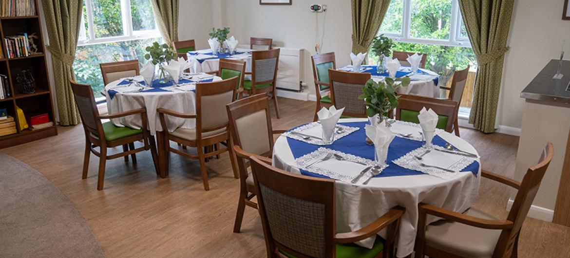 Large earth toned dining area, linking in with the outdoors from the multiple floor to ceiling windows creating a seamless link. The open space is home to multiple circular dining tables and chairs dressed for a dinner service.